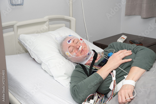 Middle aged woman measuring brain waves, examining polysomnography in sleep lab photo