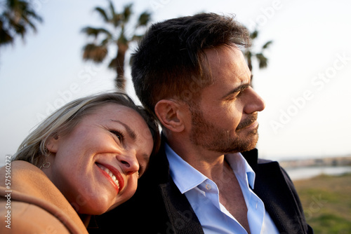 Portrait happy and relaxed couple on vacation or weekend getaway. Laughing wife leaning on husband shoulder. Loving partners enjoying a romantic trip. People looking at the horizon.