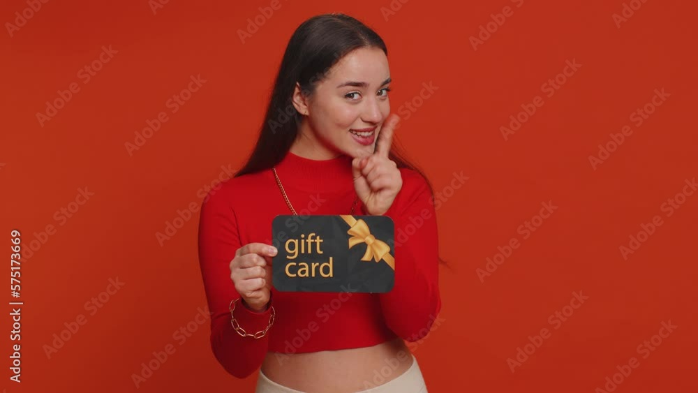 Young woman in crop top showing pointing on gift discount certificate voucher coupon for store holidays sale. Lovely girl with shopping christmas surprise card isolated alone on red studio background Young woman in crop top showing pointing on gift discount certificate voucher coupon for store holidays sale. Lovely girl with shopping christmas surprise card isolated alone on red studio background