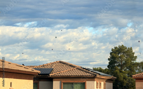Hot-air balloons free flying high above house roofs and pine trees in a cloudy sky, Phoenix, Arizona in winter