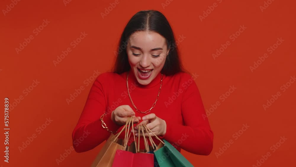Young woman in crop top showing shopping bags, advertising discounts, smiling looking amazed with low prices, shopping on Black Friday holidays. Girl indoors isolated alone on studio red background Young woman in crop top showing shopping bags, advertising discounts, smiling looking amazed with low prices, shopping on Black Friday holidays. Girl indoors isolated alone on studio red background