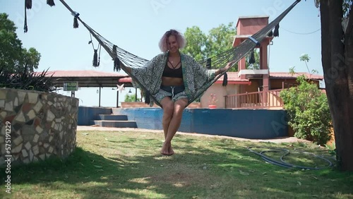 In the slow-motion video, a young woman smiles happily and swings in a hammock.