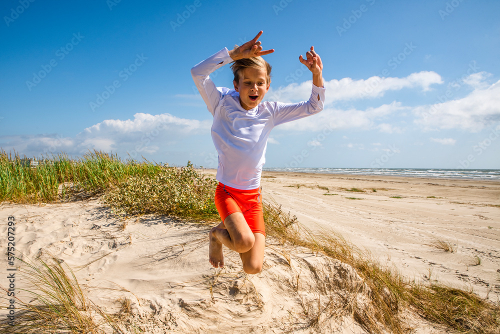 Fototapeta premium Young boy at the beach jumping from a sand dune