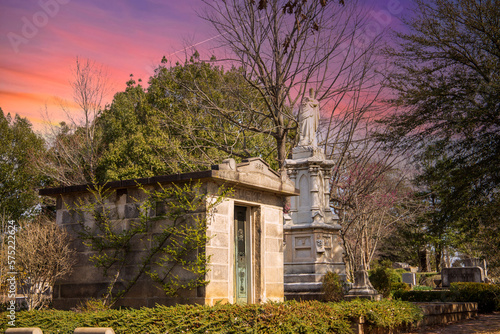 a gorgeous winter landscape in the graveyard with headstones, graves, bare trees, lush green trees, plants and flowers at the Oakland Cemetery with powerful clouds at sunset in Atlanta Georgia USA photo