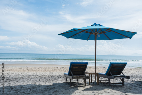 Beach chairs and umbrellas on the sand beach with cloudy blue sky background. Summer vacation travel concept.