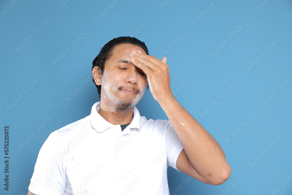 Close up portrait of young Asian man looking at camera, using facial clay mask, posing isolated over blue background. Beauty procedure and skincare routine concept. Horizontol shot Close up portrait of young Asian man looking at camera, using facial clay mask, posing isolated over blue background. Beauty procedure and skincare routine concept. Horizontol shot