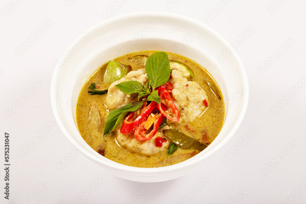 Green curry with fish balls and topped with red pepper and basil in a white bowl, coconut milk curry with green curry paste, fish ball made from Notopterus fish, very popular food in Thailand.