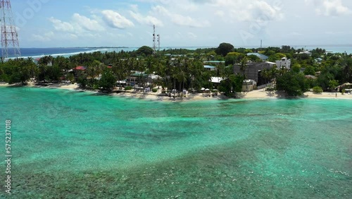 Aerial Shot Of Hotels Amidst Tropical Trees On Island, Drone Flying Backwards Over Waves In Sea - Thulusdhoo, Maldives photo