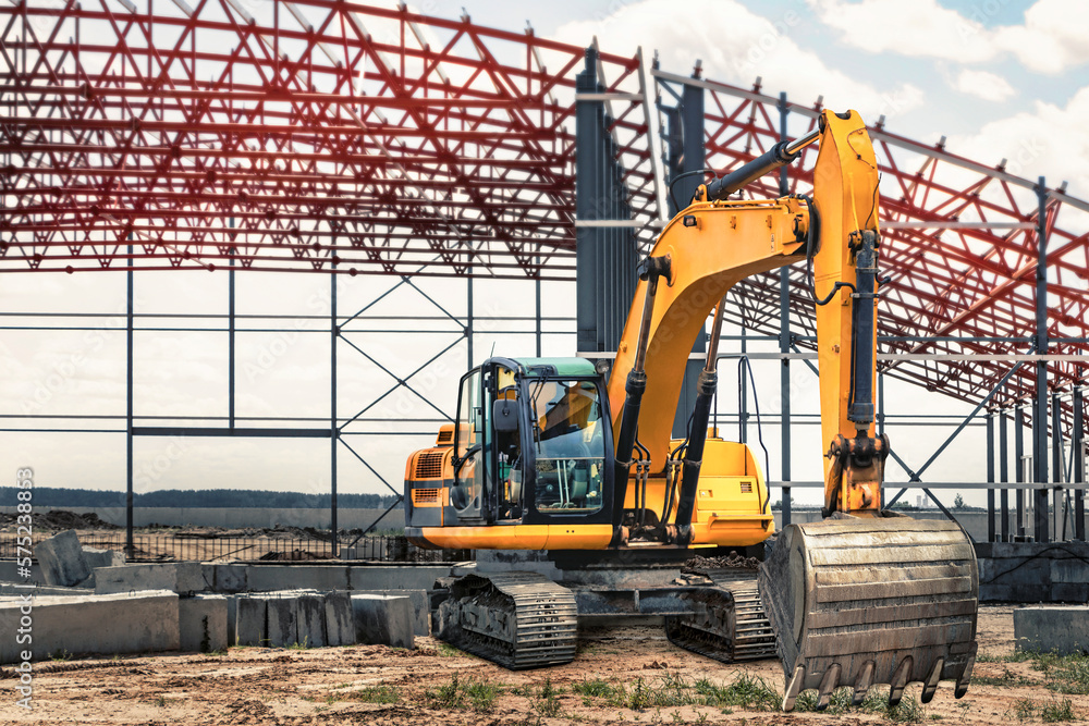 A large yellow crawler excavator at a construction site. Construction of a modern frame shop. excavation. Rental of construction equipment. Powerful construction equipment for earthworks. A large yellow crawler excavator at a construction site. Construction of a modern frame shop. excavation. Rental of construction equipment. Powerful construction equipment for earthworks.