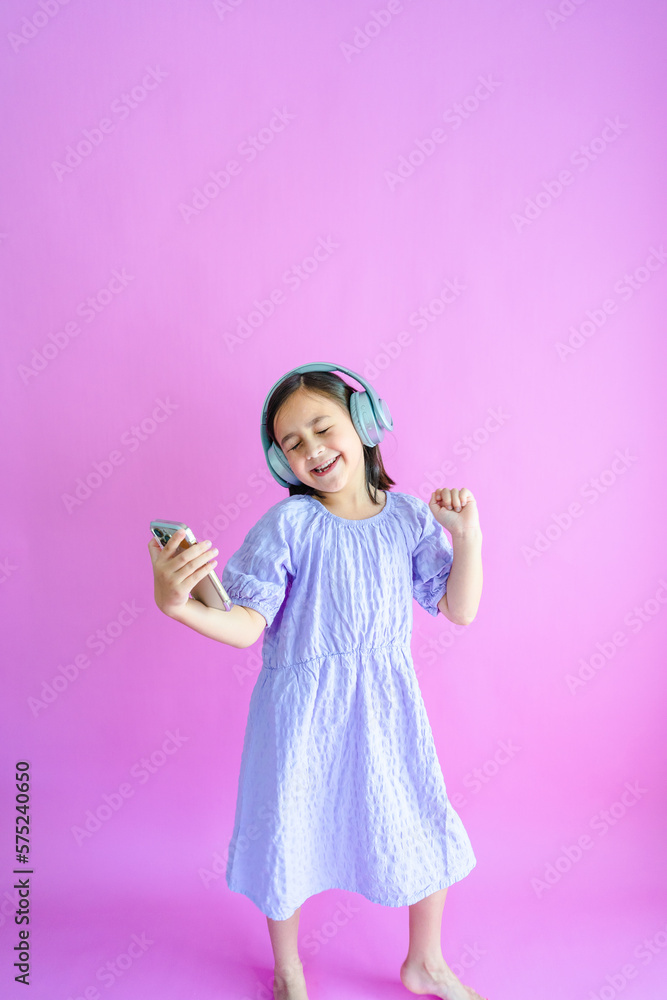 Pretty little girl holding a phone, wearing headphones, and dancing to her music. 