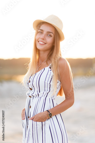 young blonde in a hat and summer dress on the beach