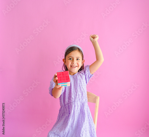 Foto Pretty little girl sitting on a chair with one side of a Rubik's cube being solved