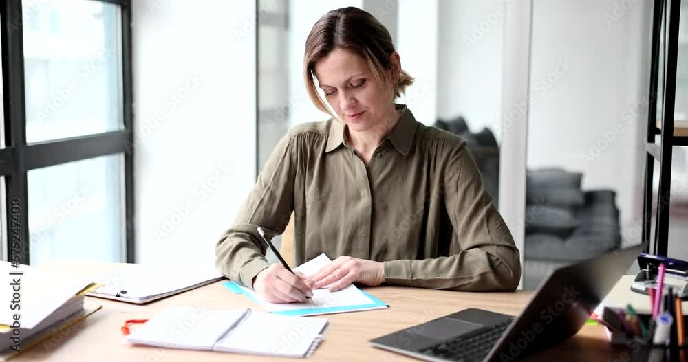 Thoughtful woman writes notes in notebook at workplace in office Thoughtful woman writes notes in notebook at workplace in office