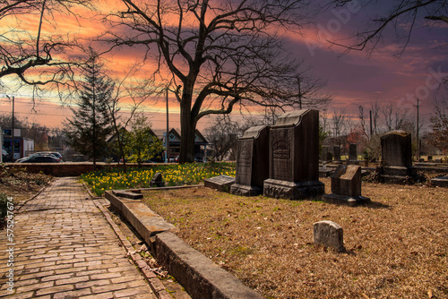 a gorgeous winter landscape in the graveyard with headstones, graves, bare trees, lush green trees, plants and flowers at the Oakland Cemetery with powerful clouds at sunset in Atlanta Georgia USA photo