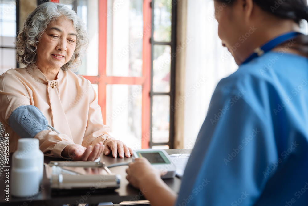 Fototapeta premium Female doctor checking old woman blood pressure at clinic and filling patient history in the morning.