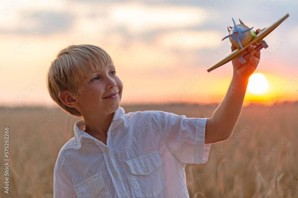 Happy child playing with a toy plane in nature during summer sunset. Boy in a white shirt with a plane in hands on wheat field. Kid holds a wooden airplane and dreams of being a pilot, on the nature Happy child playing with a toy plane in nature during summer sunset. Boy in a white shirt with a plane in hands on wheat field. Kid holds a wooden airplane and dreams of being a pilot, on the nature
