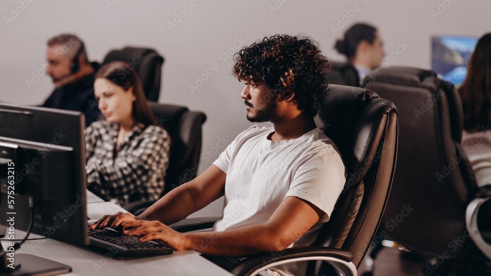 © CinemaF - Focused trade broker in the office. Concentrated young man is working with computer at his workplace. Programmer in white t-shirt typing on keyboard