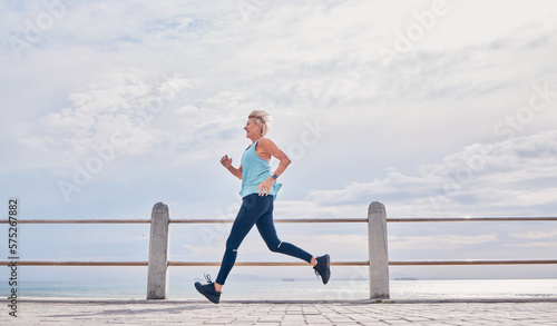 Senior woman running outdoor at on sky mockup at beach promenade for energy, health and cardio workout. Elderly female, exercise and runner at ocean for sports training, fitness and healthy marathon