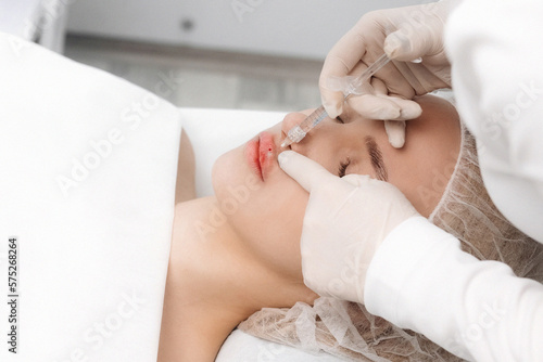 close-up  female lips. Surgeon  in medical gloves  carefully and slowly injects hyaluronic acid into woman s lips with a syringe. lip augmentation procedure. beauty injections. Plastic surgery.