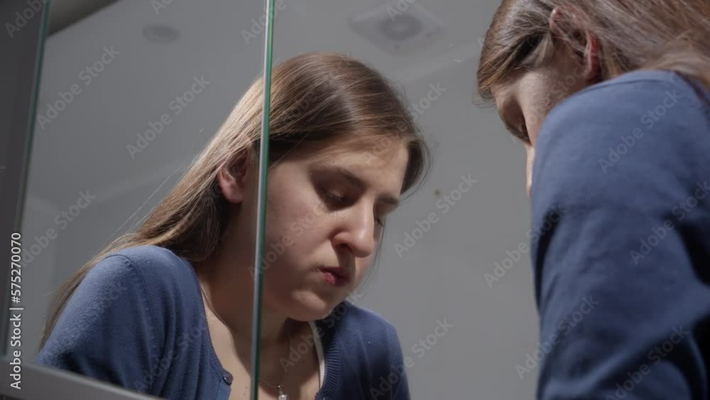 Upset young woman sighing and calming down at bathroom mirror. Concept of depression, stress, mental illness and problems, loneliness and frustration Upset young woman sighing and calming down at bathroom mirror. Concept of depression, stress, mental illness and problems, loneliness and frustration