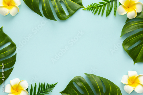 Summer background with tropical frangipani flowers and green tropical palm leaves on light background. Flat lay, top view. Summer party backdrop photo