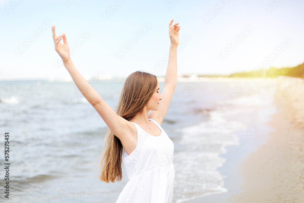 Happy smiling woman in free happiness bliss on ocean beach standing with raising hands. Portrait of a multicultural female model in white summer dress enjoying nature Happy smiling woman in free happiness bliss on ocean beach standing with raising hands. Portrait of a multicultural female model in white summer dress enjoying nature