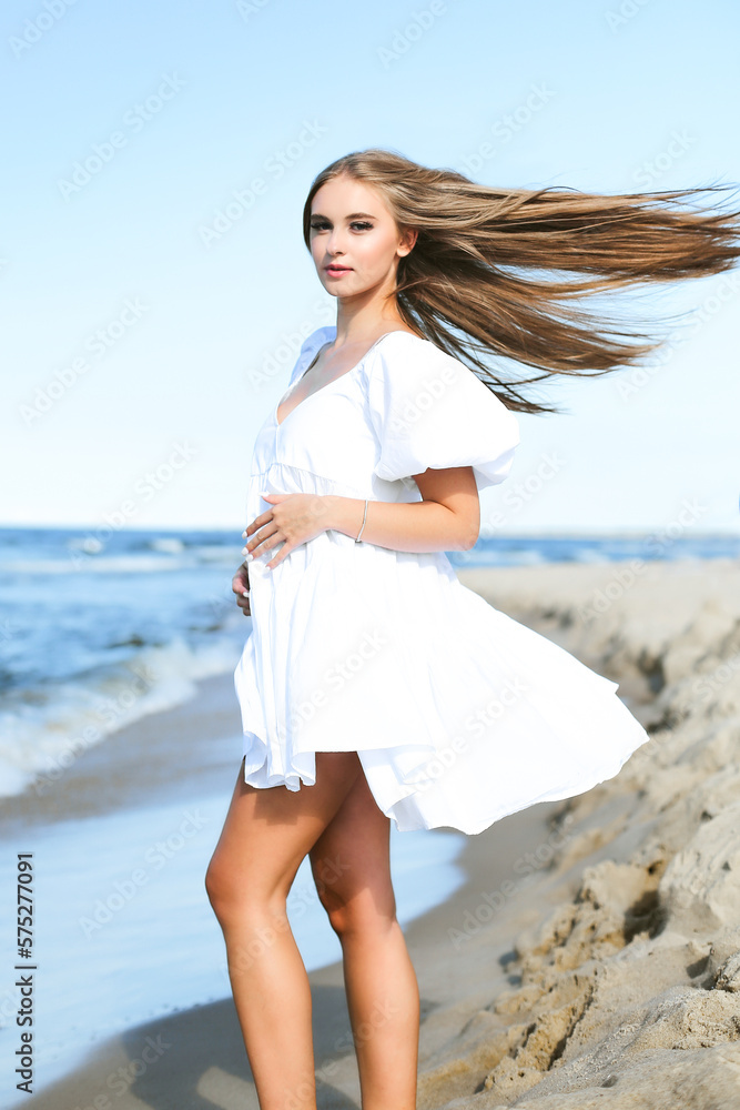 Happy, beautiful woman on the ocean beach standing in a white summer dress Happy, beautiful woman on the ocean beach standing in a white summer dress