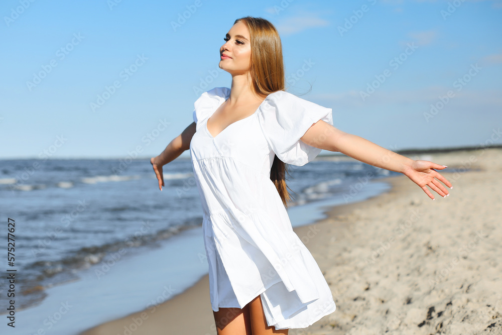 Happy, beautiful woman on the ocean beach standing in a white summer dress, open arms Happy, beautiful woman on the ocean beach standing in a white summer dress, open arms