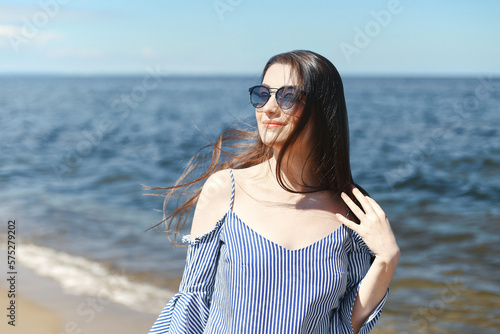 Portrait of a happy smiling brunette woman standing on ocean beach and looking at the camera