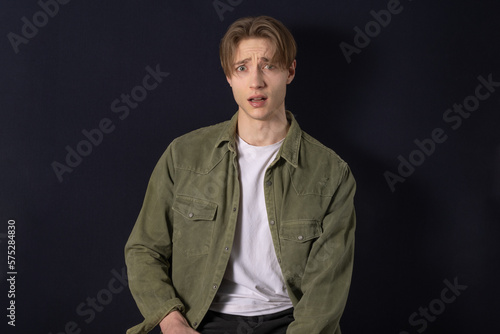 picture of male student sit on dark with blonde middle part haircut look at camera frightened and scared