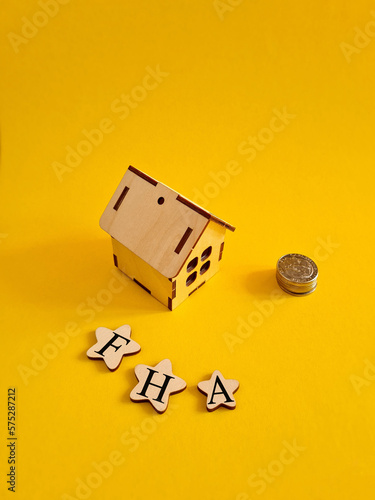 FHA federal housing administration symbol. Concept words 'FHA federal housing administration ' on wooden stars on a beautiful yellow background. Model of house. Business and FHA concept. Copy space.