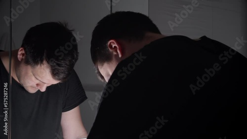 Young angry man breathing deeply and looking in his reflection in mirror. Concept of depression, suicide, stress, mental illness, loneliness and frustration