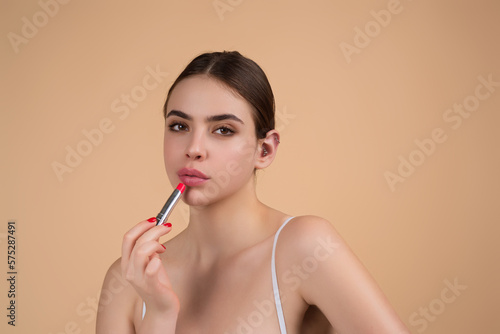 Beautiful young woman applying red lipstick on lips, studio color background. Sexy girl applied lipstick. Young nodel holding pink lipstick. Red lips make up. Beautiful woman putting lipstick on lips.