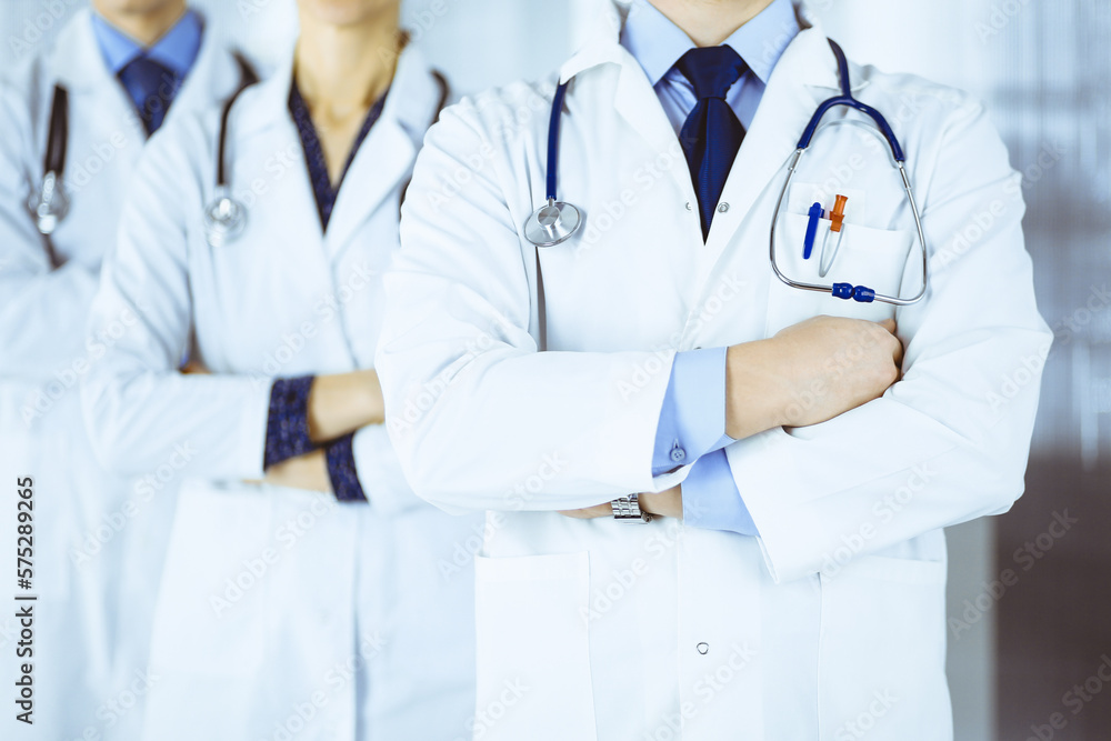 Group of modern doctors standing as a team with crossed arms and stethoscopes in hospital office. Physicians ready to examine and help patients. Medical help, insurance in health care Group of modern doctors standing as a team with crossed arms and stethoscopes in hospital office. Physicians ready to examine and help patients. Medical help, insurance in health care