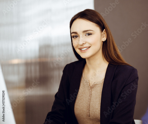 Young beautiful business woman is talking to her colleague, while sitting at the desk in a modern office. Concept of business success