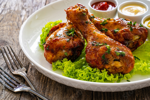 Barbecue chicken drumsticks with lettuce, ketchup, mayonnaise and mustard on wooden table 