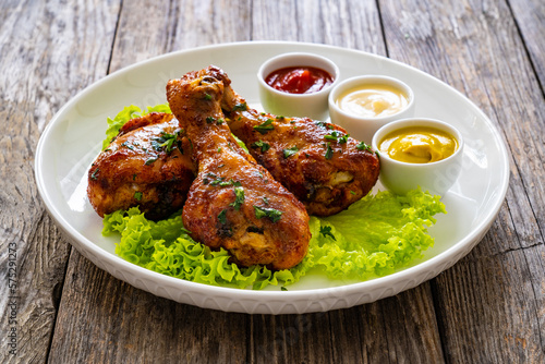 Barbecue chicken drumsticks with lettuce, ketchup, mayonnaise and mustard on wooden table
