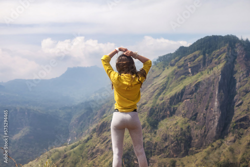 Rear view pretty woman in front of Sri Lankan mountains in sight landmark nature background. Cute lady posing from behind enjoying at tropical journey, Ella, Sri Lanka. Copy advertising text space