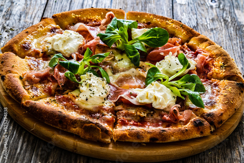 Circle prosciutto pizza with mascarpone cheese and leafy greens on wooden table 