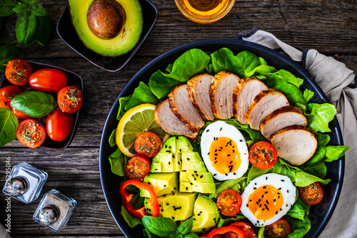 Tasty salad - roasted veal loin, avocado, boiled eggs and fresh vegetables on wooden table 