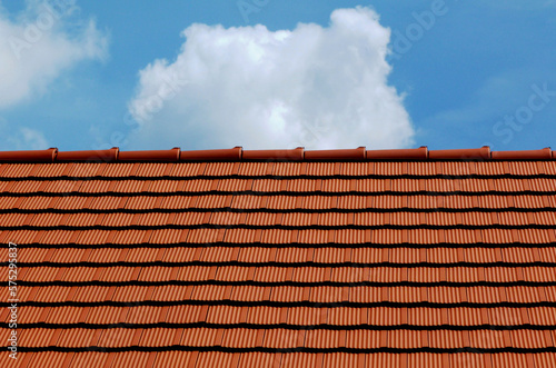 sloped red clay roof ridge detail. new bright clay house roof tiles. construction industry and building materials concept. clear blue sky. bright sunlight