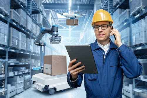 Manager with digital tablet and phone in an automated warehouse with robots and drones