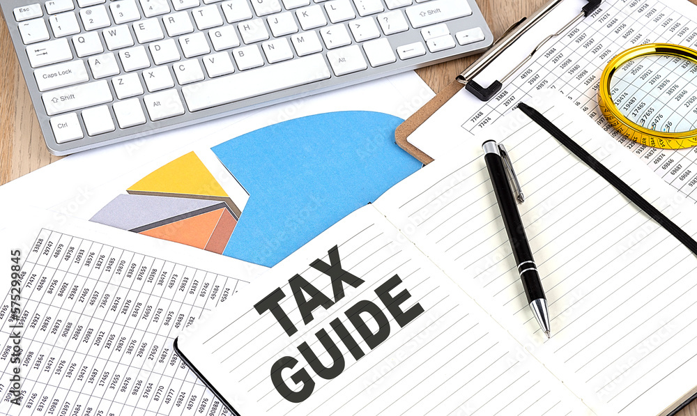 TAX GUIDE text on notebook with chart and keyboard TAX GUIDE text on notebook with chart and keyboard