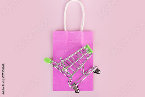 gift bag, bright shopping bag with supermarket trolley on pink background, online shopping, top view