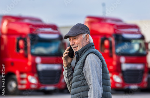 Senior man talking on phone in front of trucks