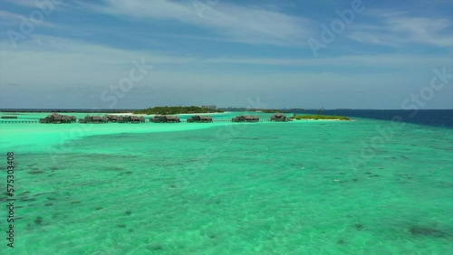 Aerial: Panning Shot Of Luxurious Resorts On Turquoise Sea, Drone Flying Forward During Sunny Day - Thulusdhoo, Maldives photo