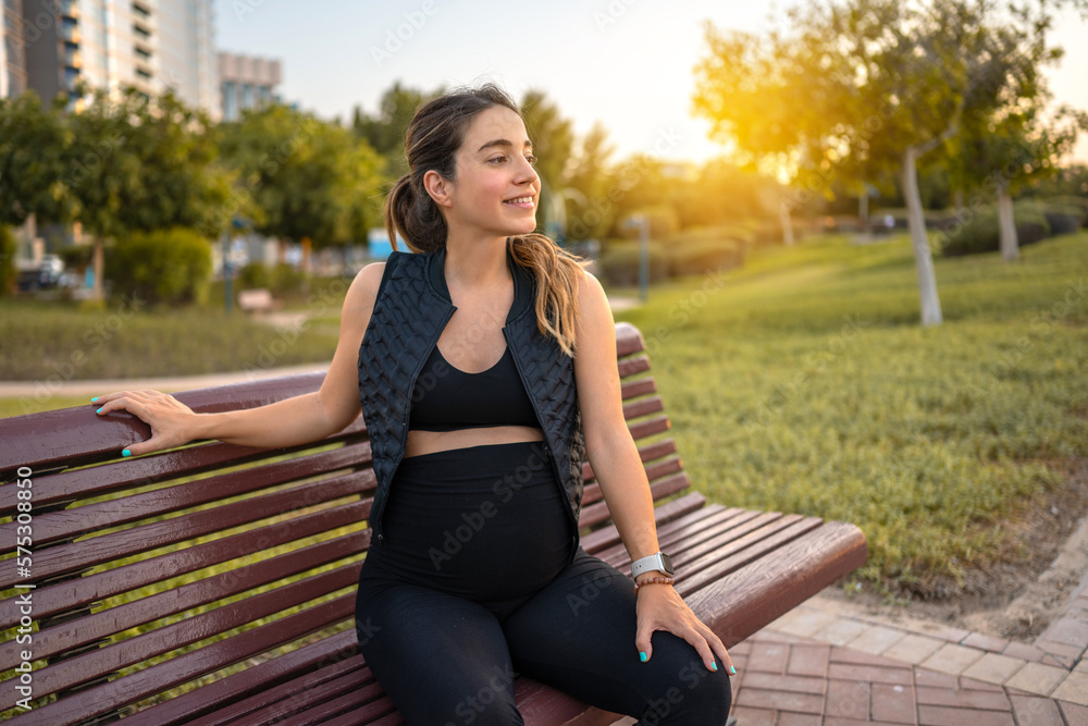 Portrait of smiling young pregnant woman resting on wooden park's bench during sunset Portrait of smiling young pregnant woman resting on wooden park's bench during sunset