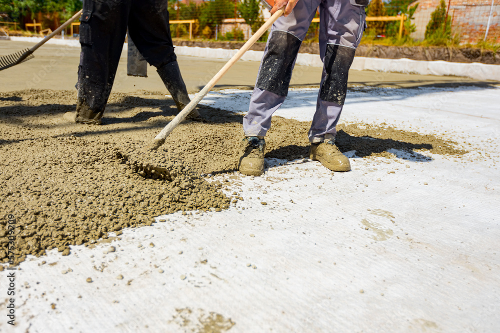 Rigger, worker is using rake to level fresh concrete into building foundation over reinforcing steel bars Rigger, worker is using rake to level fresh concrete into building foundation over reinforcing steel bars