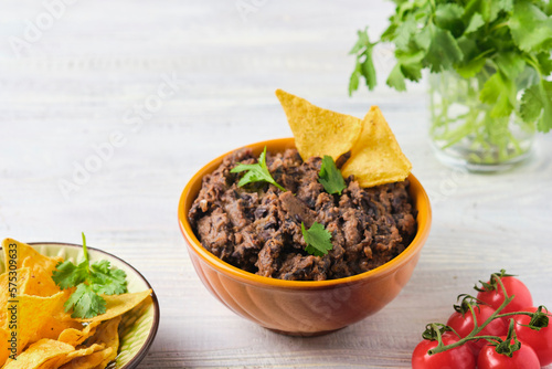 Refried beans, a dish of black beans, fried onions and spices in a yellow ceramic bowl on a light wooden background. Bean dishes. Vegan, lenten food.