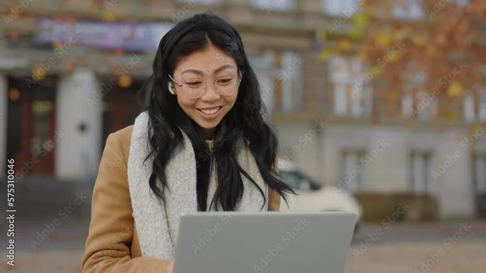 Smiled Attractive Asian Student Sitting in the Bench near University, Using Laptop, Having Distant Lecture, Waving at the Camera Using Earphones. Girl Studying Online. People and Technology Concept Smiled Attractive Asian Student Sitting in the Bench near University, Using Laptop, Having Distant Lecture, Waving at the Camera Using Earphones. Girl Studying Online. People and Technology Concept